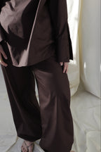 Woman wearing a pure cotton brown balloon trousers by Kureé The Brand Womenswear, standing against a draped backdrop.