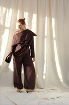 Woman wearing a pure cotton brown off-shoulder top and balloon trousers by Kureé The Brand Womenswear, standing against a draped backdrop.