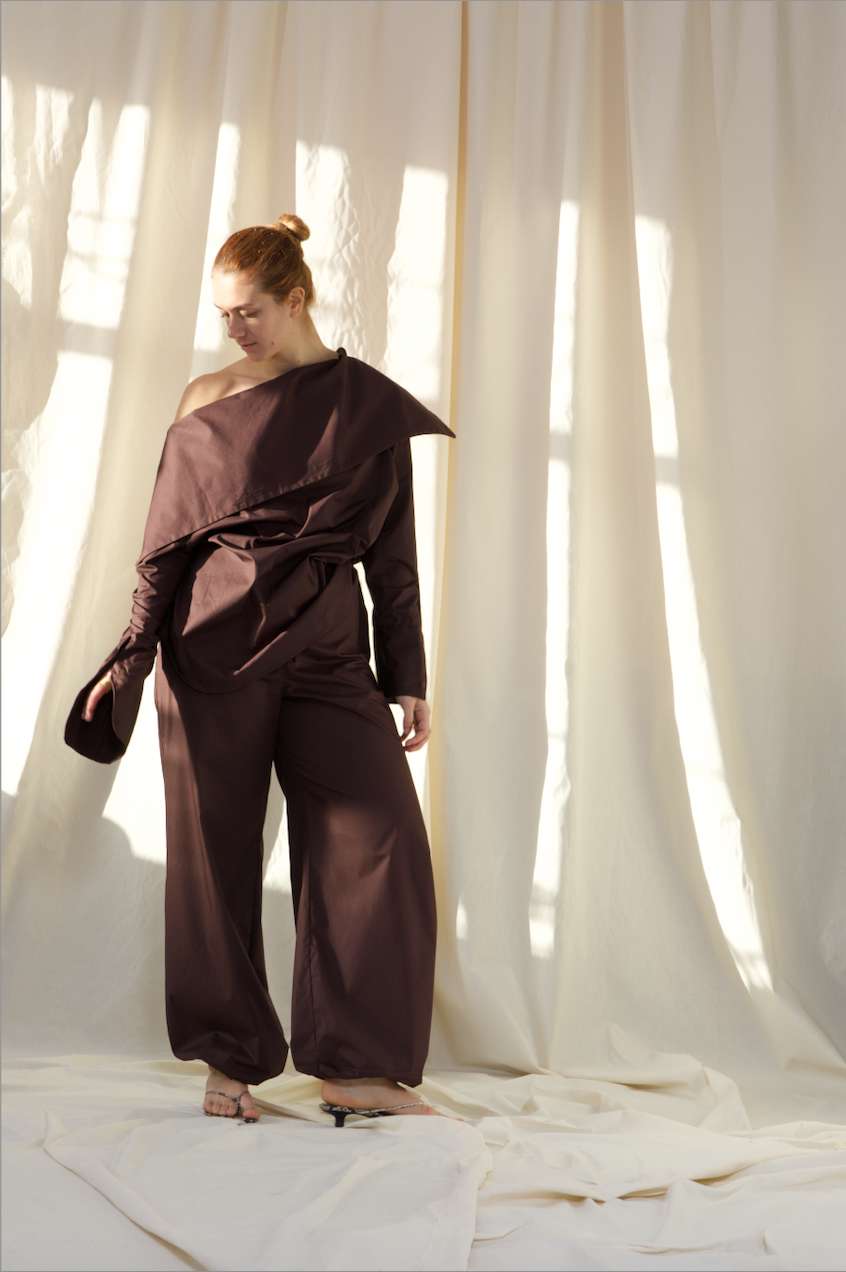 Woman wearing a pure cotton brown off-shoulder top and balloon trousers by Kureé The Brand Womenswear, standing against a draped backdrop.