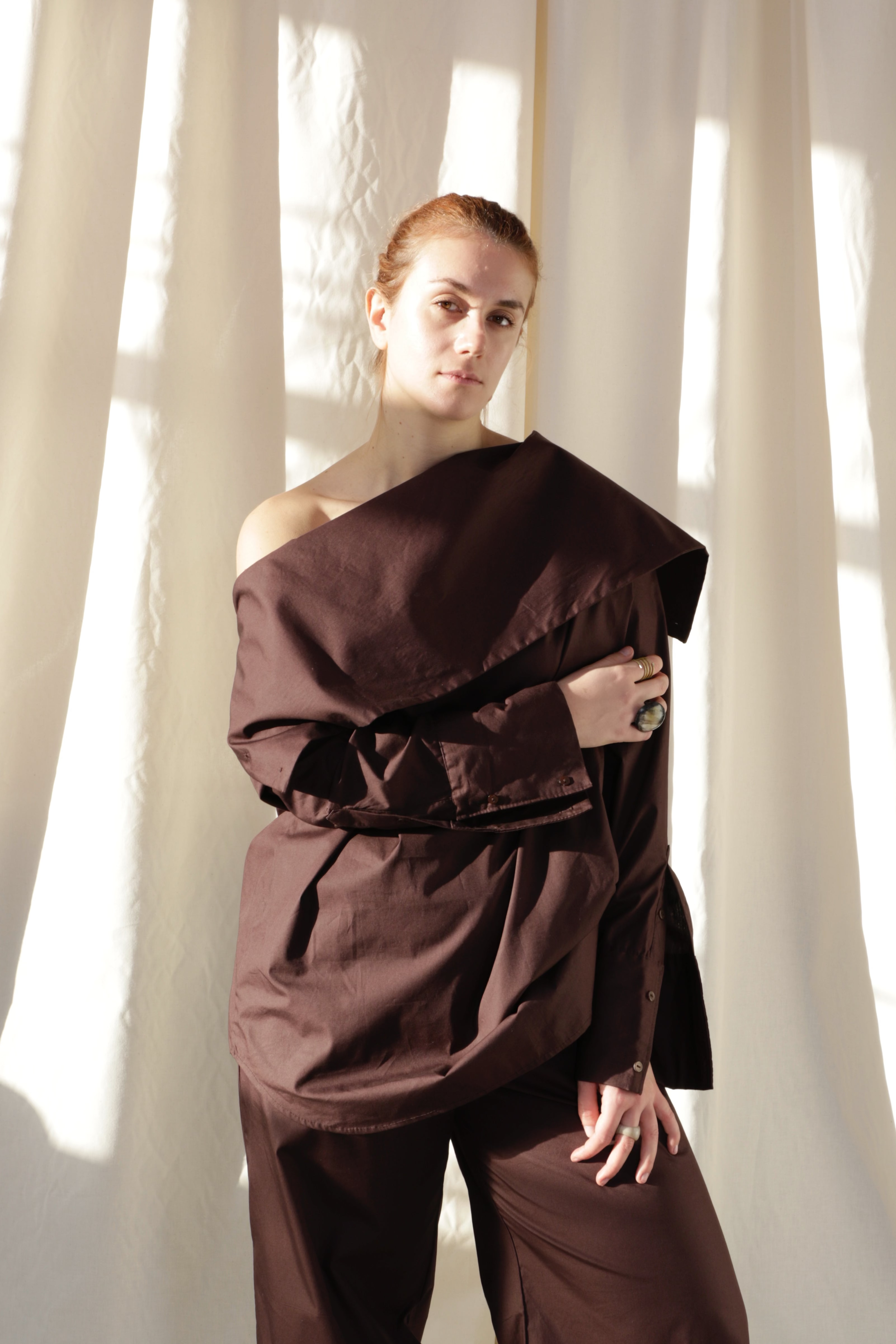 Woman wearing a pure cotton brown shirt by Kureé The Brand Womenswear standing against a draped backdrop