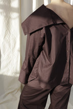 Woman wearing a pure cotton brown shirt by Kureé The Brand Womenswear standing against a draped backdrop