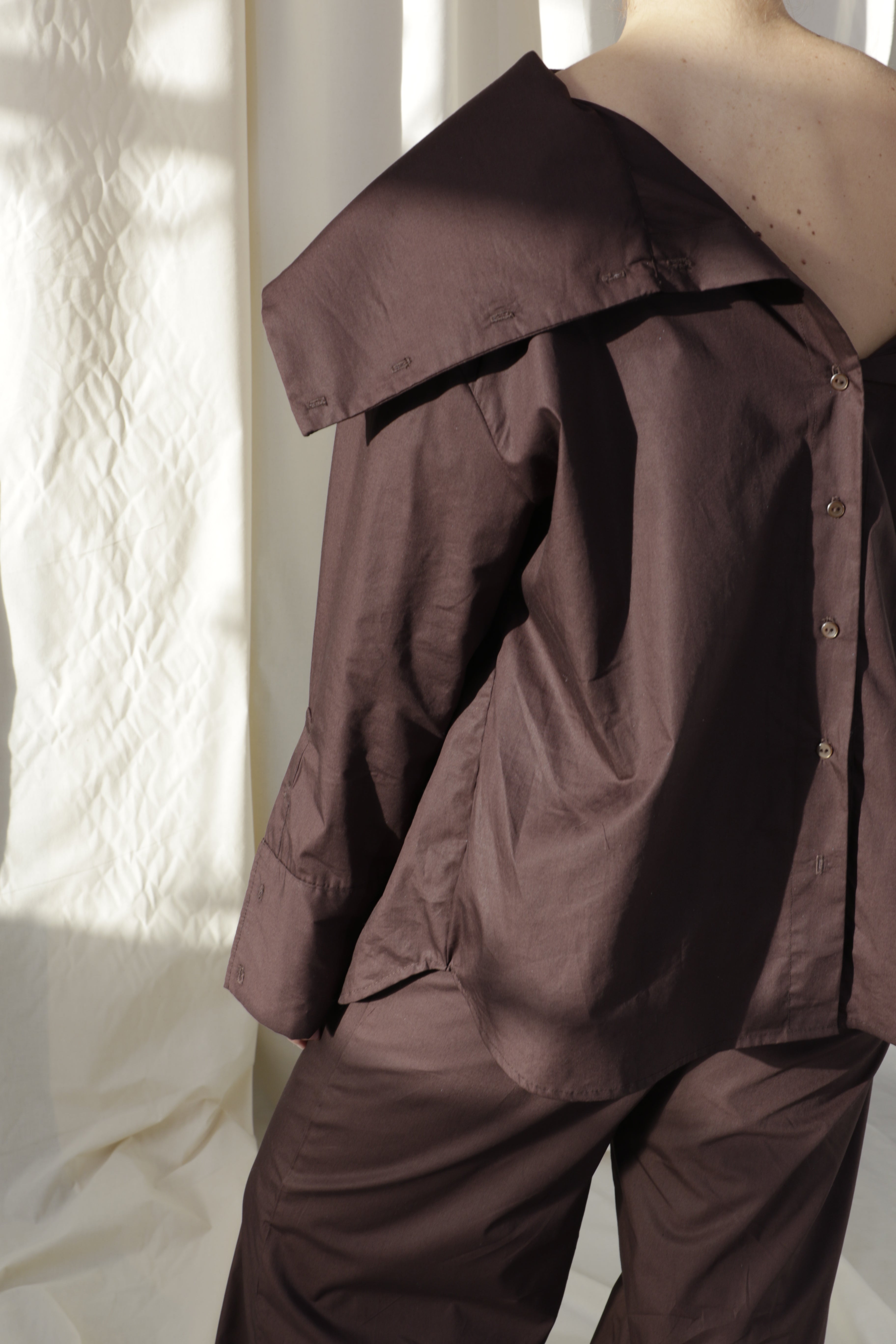 Woman wearing a pure cotton brown shirt by Kureé The Brand Womenswear standing against a draped backdrop
